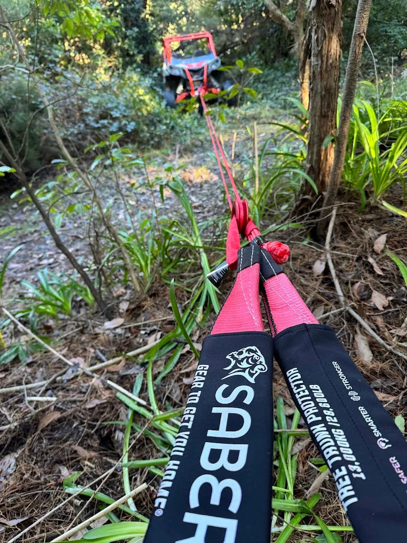 Saber tree trunk protector strap rigged in the foreground with a small stuck 4WD visible in the bush behind