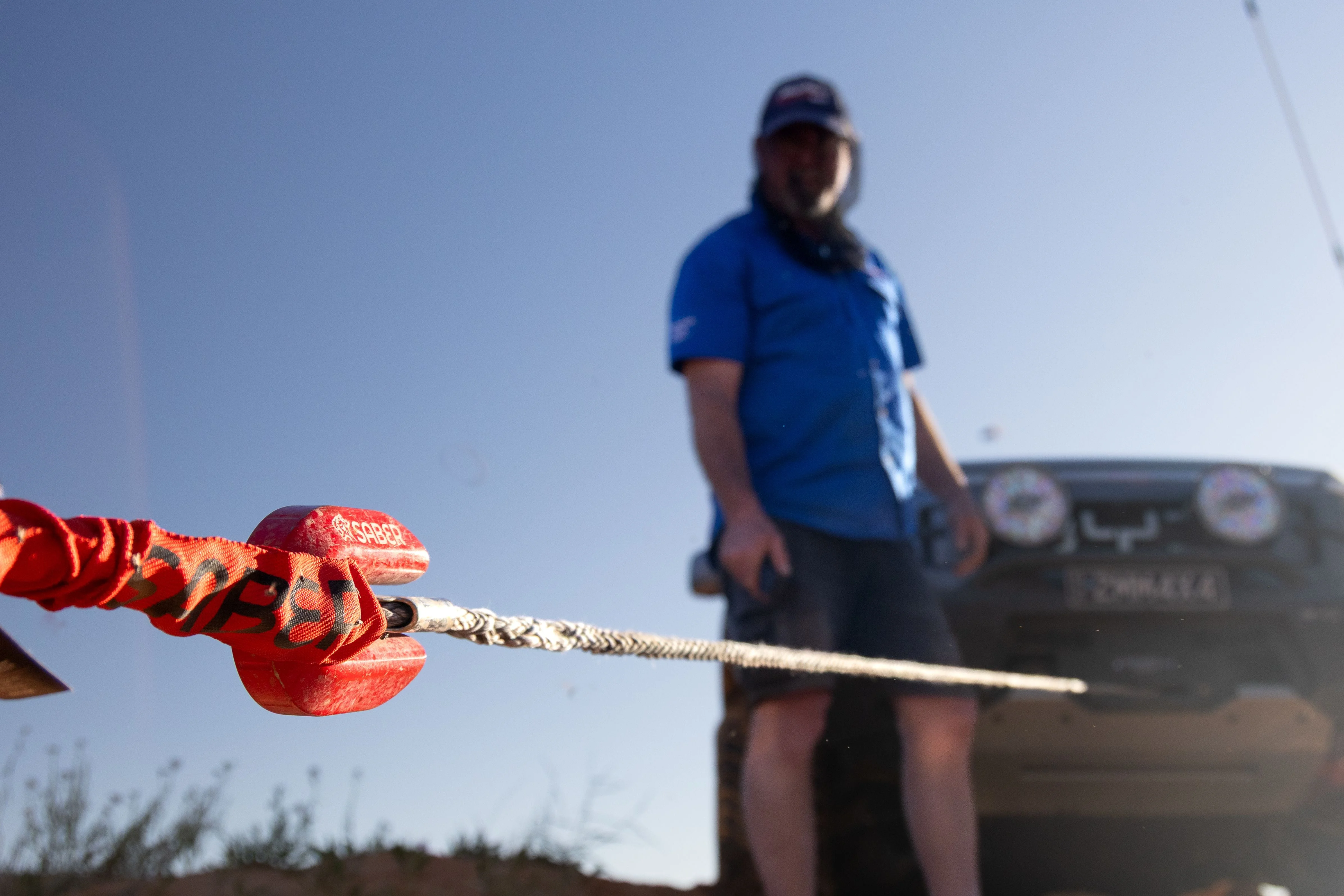 Red Saber soft shackle held up close to camera with a person and 4WD standing out of focus in the outback background