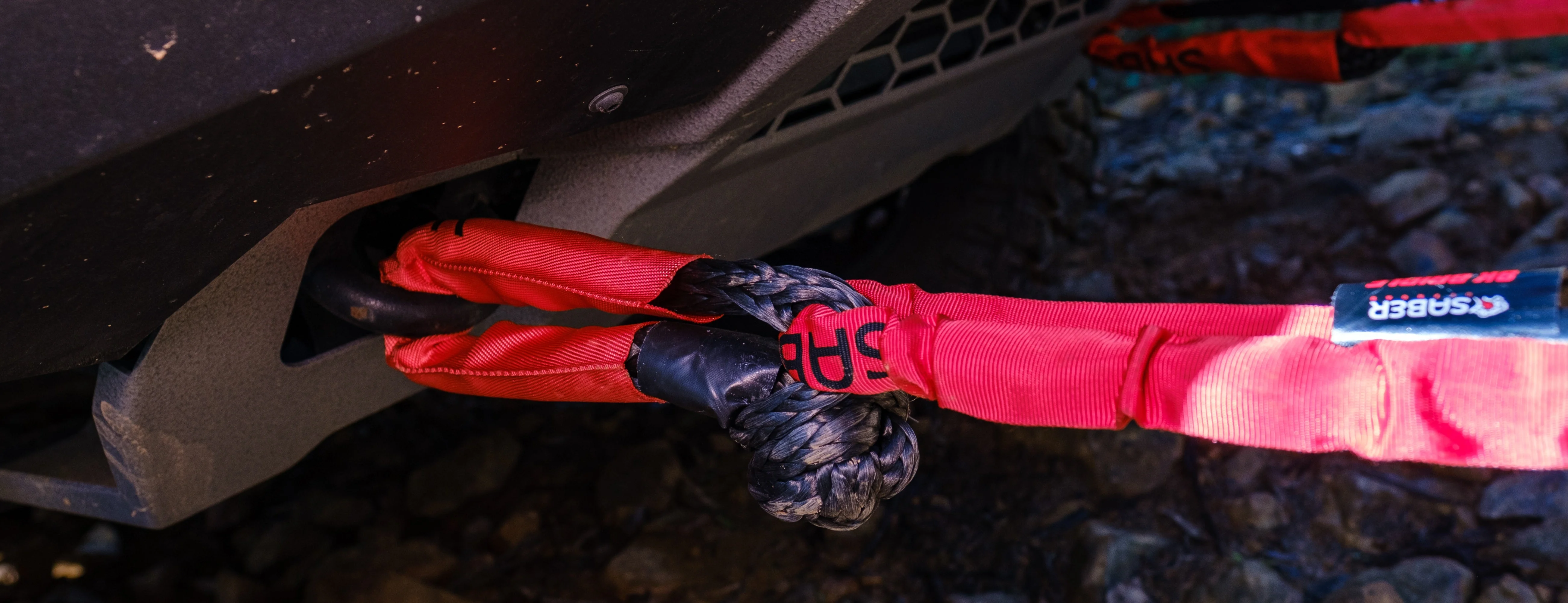 Wide shot of a red Saber Sheath soft shackle rigged through an Ineos Grenadier's recovery loop, branding visible on the sheath