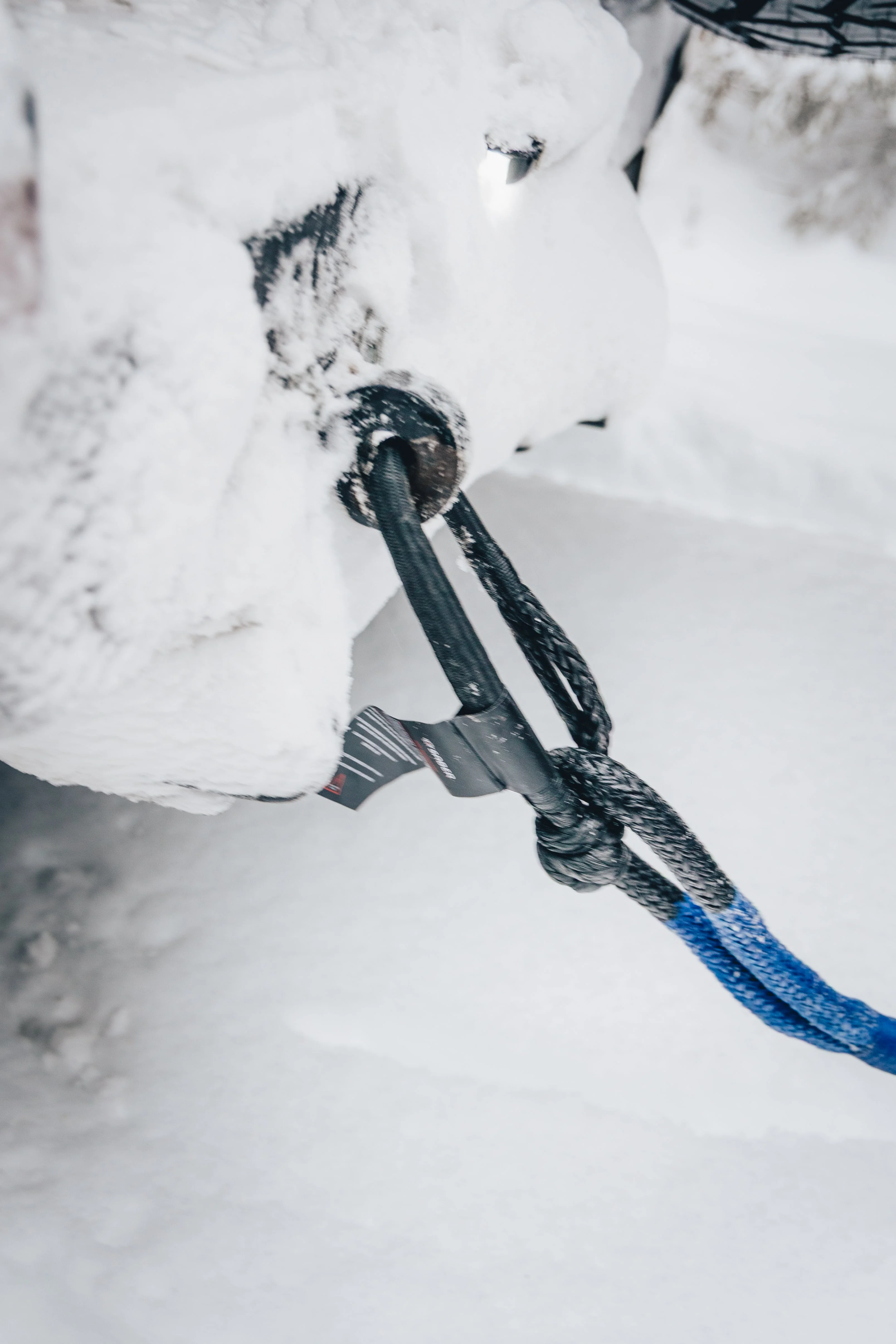Close-up of a soft shackle connecting a kinetic rope to a snow-covered vehicle's recovery point